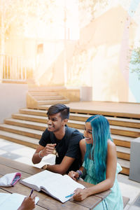 Happy friends studying while sitting outdoors