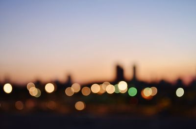 Defocused image of illuminated lights against sky during sunset