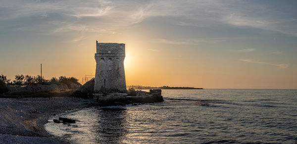 Scenic view of sea and an annient tower against sky during sunset 