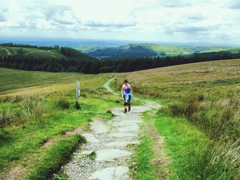 Woman walking on footpath amidst landscape against sky