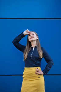 Young woman standing against blue wall