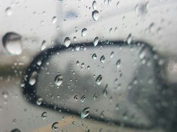 Close-up of wet glass window against sky