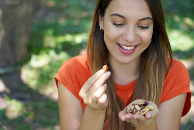 Close-up of healthy smiling woman eating brazil nuts in the park. looks at nuts.