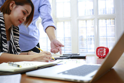 Businesswoman working while male colleague using calculator at desk in office