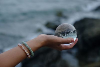 Close-up of hand holding crystal ball against sea