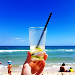 Cropped hand of woman holding drink at beach against sky