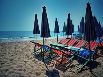 Deck chairs on beach by sea against sky