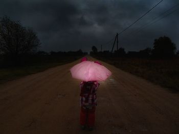 Person standing on field by road against storm clouds
