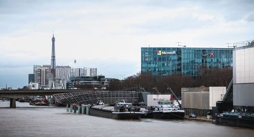 Modern buildings by river against sky in city