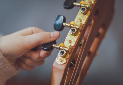 The girl twists the guitar peg while tuning the strings.