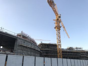 Low angle view of crane by building against sky