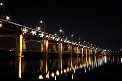 Illuminated bridge over river against sky at night