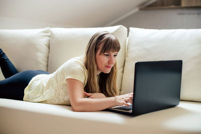 Young woman using phone while sitting on sofa at home