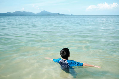 Rear view of a boy swimming in sea against distant island
