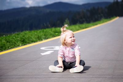 Full length of girl looking away while sitting on road
