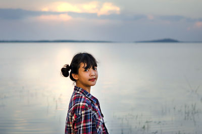 Side view portrait of girl standing against lake during sunset