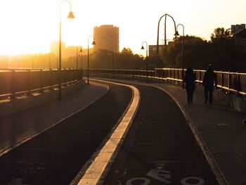 People walking on sidewalk of bridge during sunrise