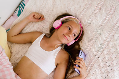 Pretty caucasian girl holds a smartphone in her hand and listens to music in wireless pink headphone