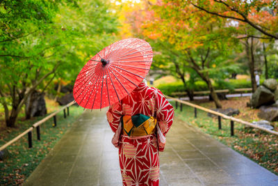 Young girls tourist wearing red kimono and umbrella took a walk in the park in autumn season 