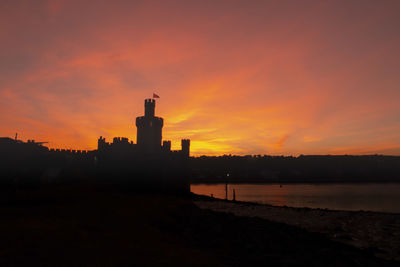 Silhouette buildings by sea against sky during sunset