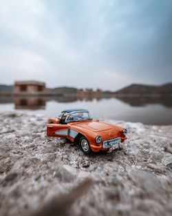 Toy car on rock by lake against sky