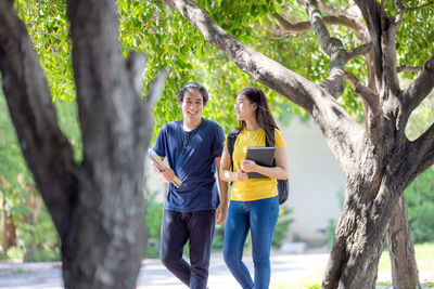 A couple of thai high school students smile while going through the woods with a book in their