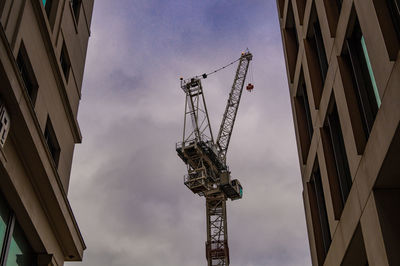 Low angle view of crane by building against sky