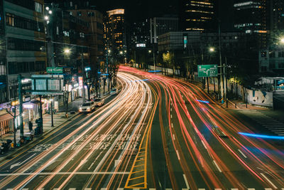 Light trails on city street amidst buildings at night