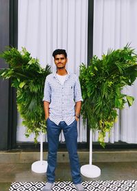 Full length portrait of young man standing in potted plant