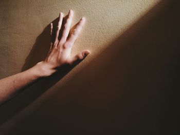 Sunlight falling on cropped hand touching wall