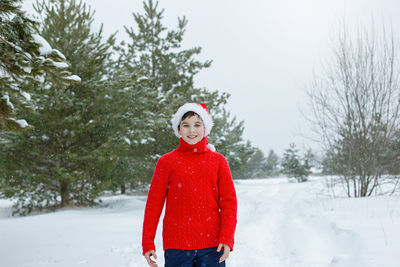 Teenager in a red sweater and a red hat stands in the winter in the park