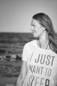 Woman looking away while standing at beach against clear sky