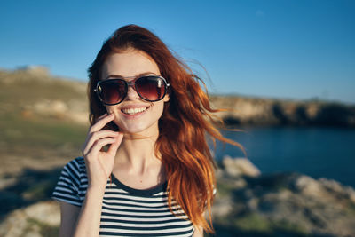 Portrait of smiling young woman using smart phone against sky
