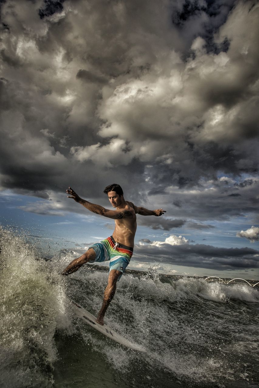 cloud - sky, sea, sky, water, beach, real people, full length, shirtless, one person, men, lifestyles, young men, sand, nature, outdoors, strength, leisure activity, day, young adult, exercising, healthy lifestyle, motion, storm cloud, horizon over water, wave, beauty in nature, sportsman, people