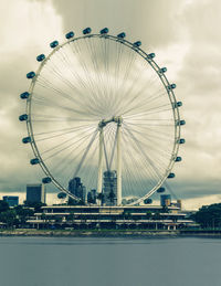 Ferris wheel in city against cloudy sky