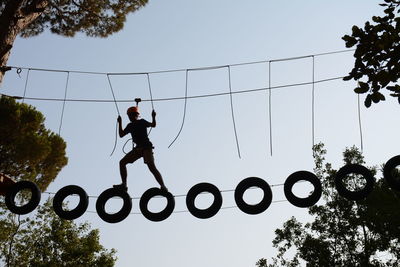 Low angle view of silhouette man on rope course against clear sky