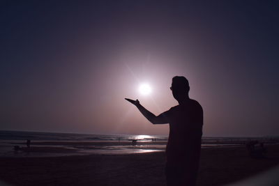 Silhouette man standing on beach against clear sky during sunset