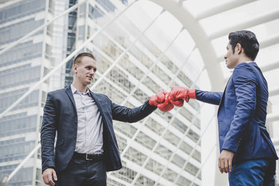 Businessman giving fist bump while standing against metallic structure