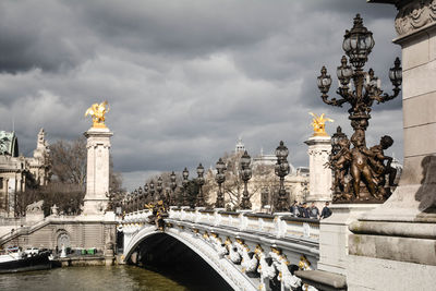 Statue on bridge against cloudy sky