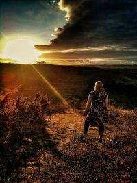 Rear view of woman on field against sky during sunset