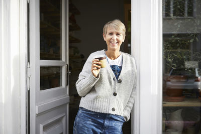 Confident mature woman having coffee at entrance of art studio