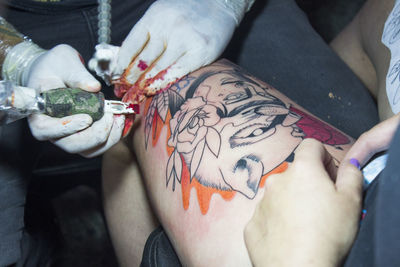 Artist tattooing on thigh of woman at studio