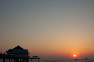 Silhouette built structure by sea against orange sky