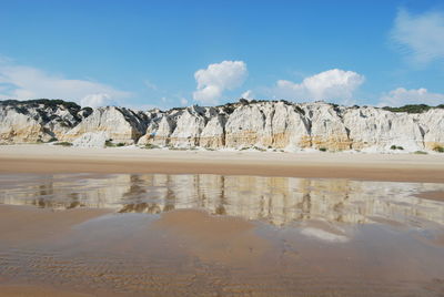 Scenic view of rocky mountains at beach against sky