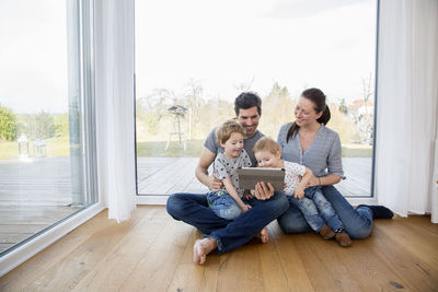 Happy family sitting on floor, using digital tablet