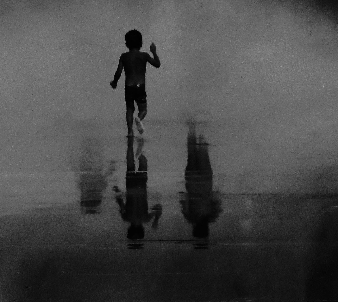 REFLECTION OF MAN STANDING IN SEA AGAINST SKY