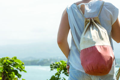 Midsection of woman carrying backpack walking against sky on sunny day