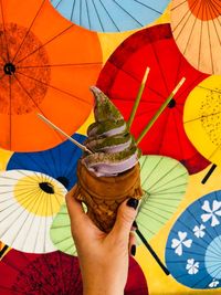 Cropped hand holding ice cream against colorful umbrellas