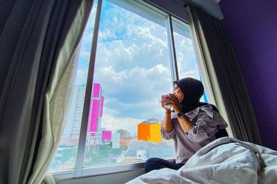 Side view of woman looking through window at home