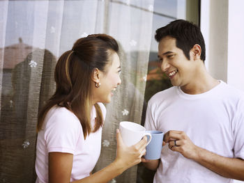 Smiling couple talking while having coffee against wall